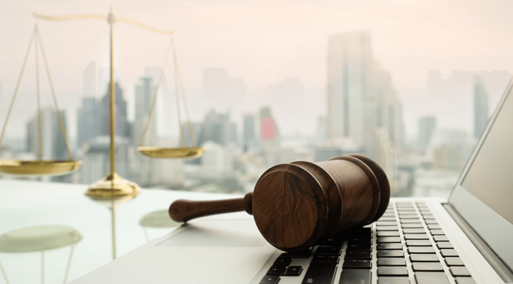 A gavel on top of a computer with a judges scale to the right. City skyscraper line is in the background.