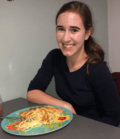 Alt-Text: A smiling Brielle sitting in front of a plate of pasta.