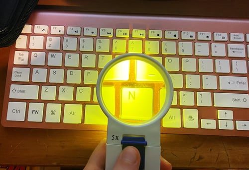 Alt-Text: My amber-lit magnifying glass held up over my keyboard