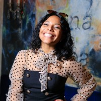 Picture of Mariella smiling broadly and confidently. She has dark black hair, tan skin and is wearing a black and white polka dot blouse with a bow.