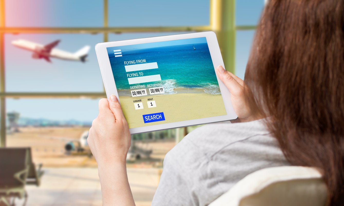 A woman sitting at an airport checking flight information, including dates, airport location, and number of passengers.