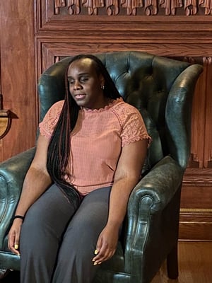 Photo of Zulay seated in a leather executive chair. She is a black woman with black hair and is dressed business casual in a peach blouse and gray slacks. 