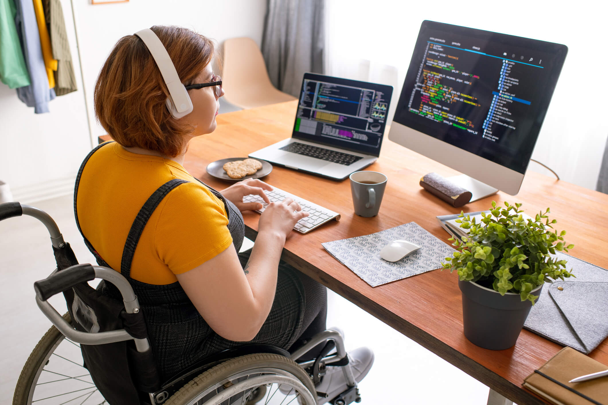 A professional woman in a wheelchair using a computer with multiple monitors, showcasing workplace accessibility for individuals with disabilities.