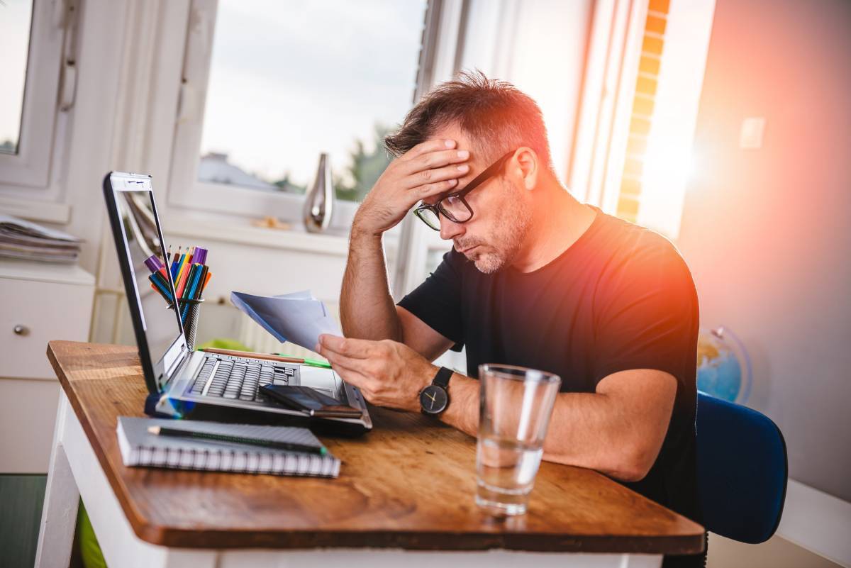 man with his hand on his head sitting at a laptop 