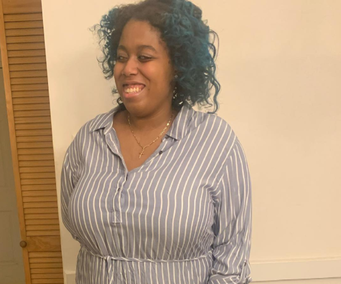 picture of the author, Lily Mordaunt, a black woman with short black hair and blue partial highlights wearing a blue button down blouse and gold necklace, smiling. 