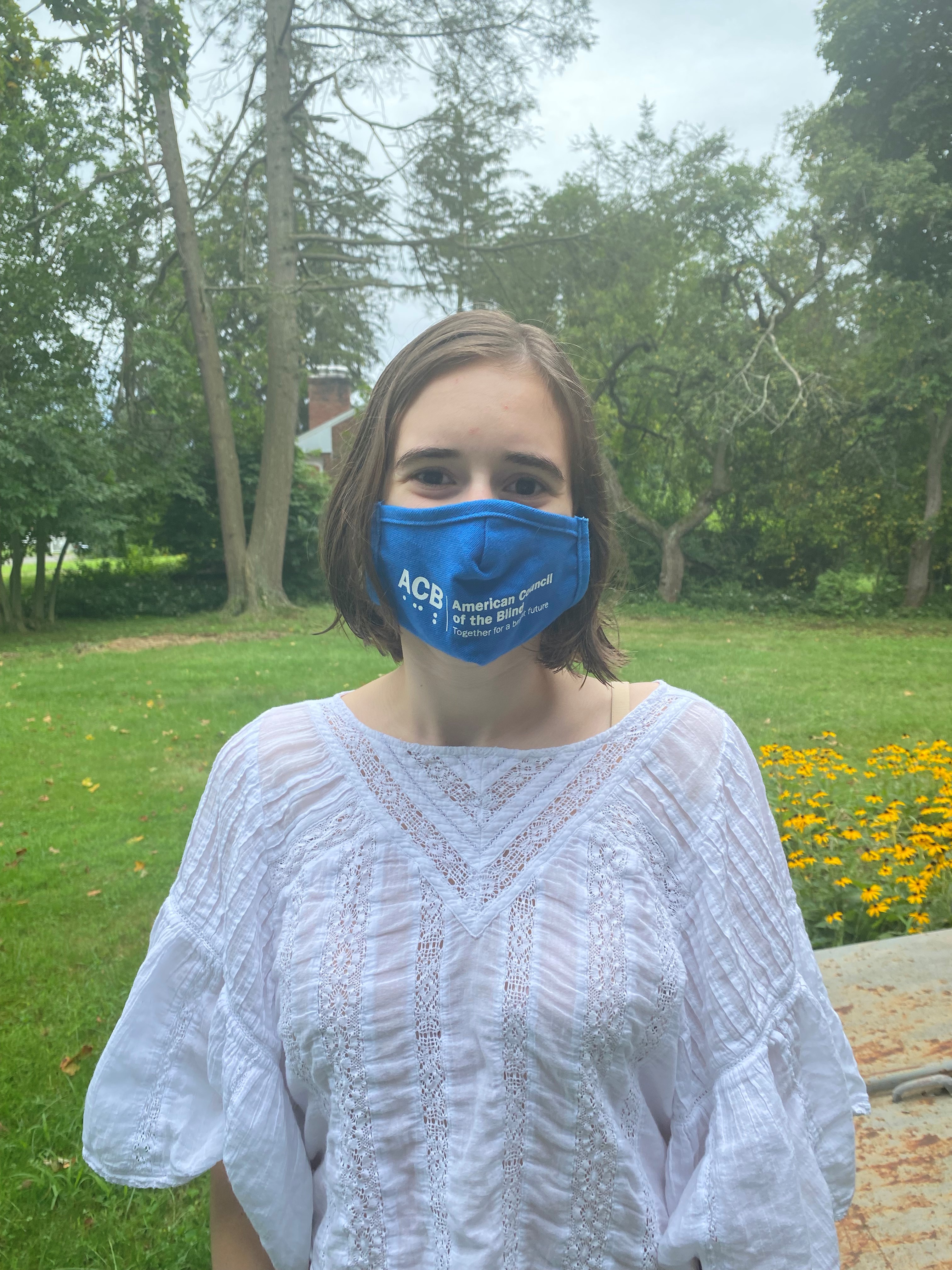 The young female author wearing a blue mask that reads "American Council of the Blind" in white text and Braille characters